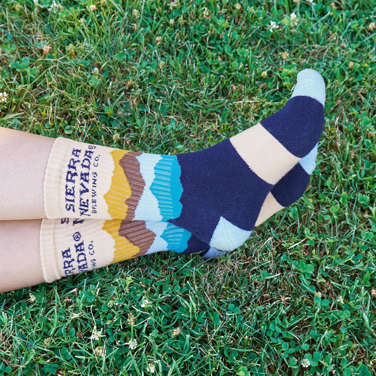 A person wears a pair of Sierra Nevada Mountain Range Socks outside in a grassy field