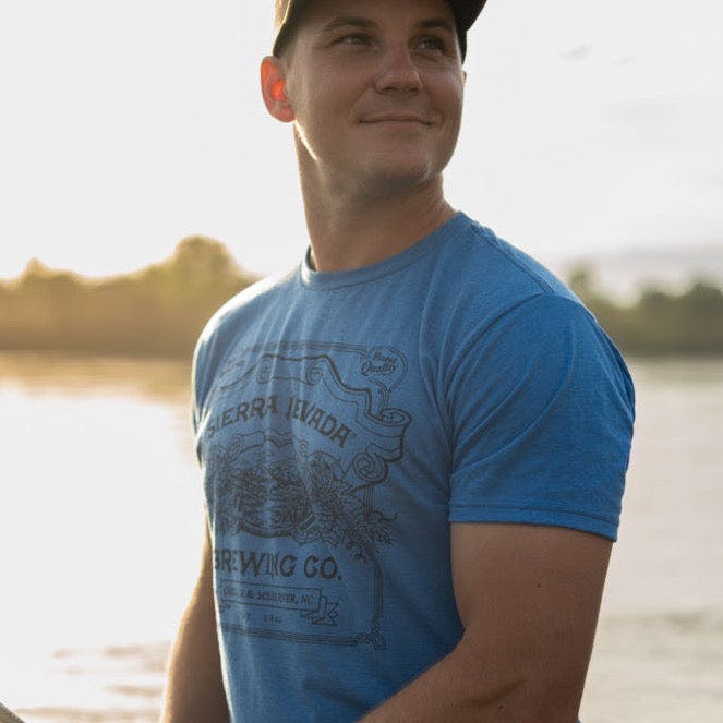 A man wears the Sierra Nevada Brewing Co. Handcrafted T-Shirt while fishing along the riverbank.