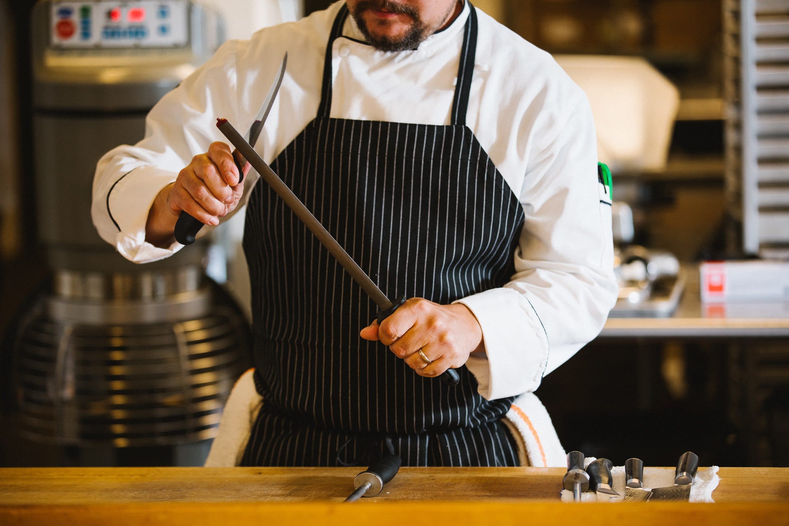 Male employee in restaurant kitchen sharpening knives