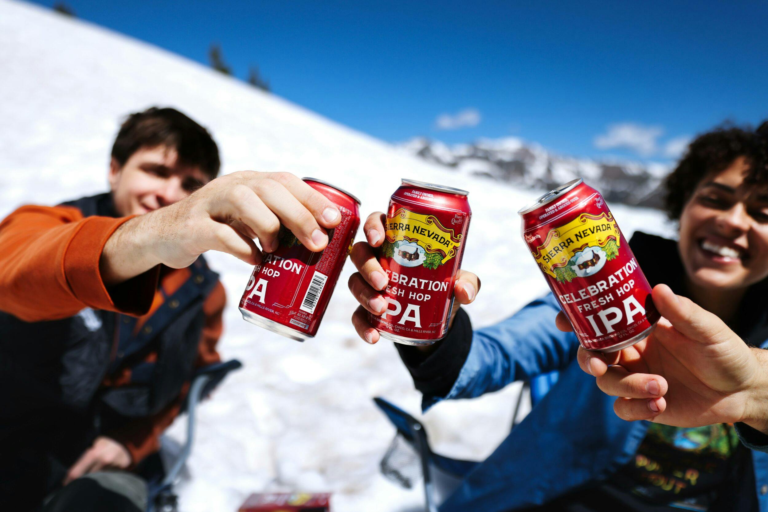 Celebration Ale cans being cheersed by friends in the snow